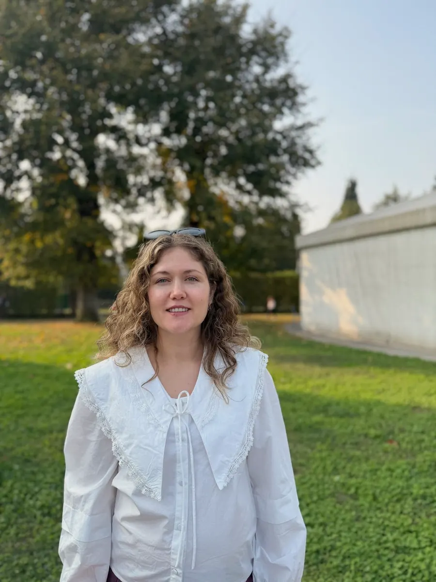 Didem Sümer Tiryaki outdoors in a white blouse, with trees and grass behind her